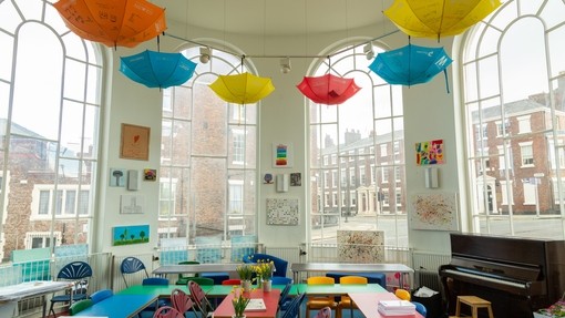 A classroom with large bay windows and colourful displays on the wall and umbrellas hanging from the ceiling 