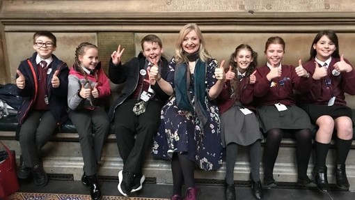 A group of students sitting Parliament with their teacher holding their thumbs up