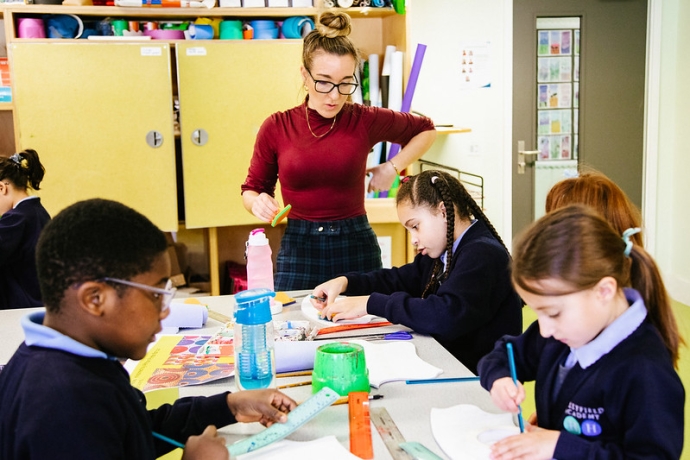 A group of primary children are at a table surrounded by art materials looking down and painting 