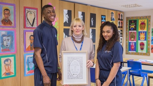 Pupils standing in a room with teacher. Art work is displayed on the wall and they are holding an Artsmark Award certificate 