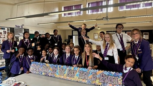 A group of Year 7 and 8 students in school uniform smiling while standing round a mosaic.