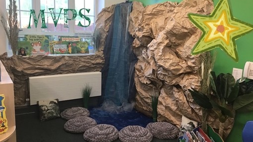 A reading area in the corner of a room that has been created to look like a waterfall with cushions for children to sit on 