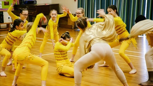 An image of a group of young girls stood in a circle wearing bright yellow. They're waving their arms and dancing. 