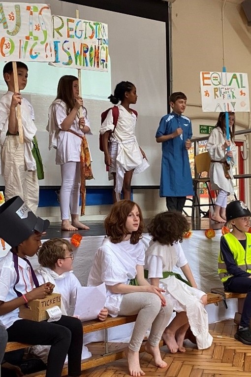 Year 4 performance about the life of Ghandi. A group of children stand on a stage in different coloured robes. 