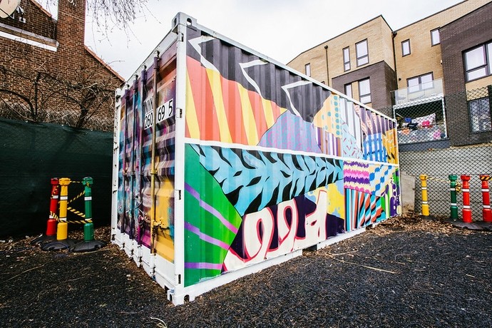 A shipping container has been painted with graffiti art, in the grounds of a school 