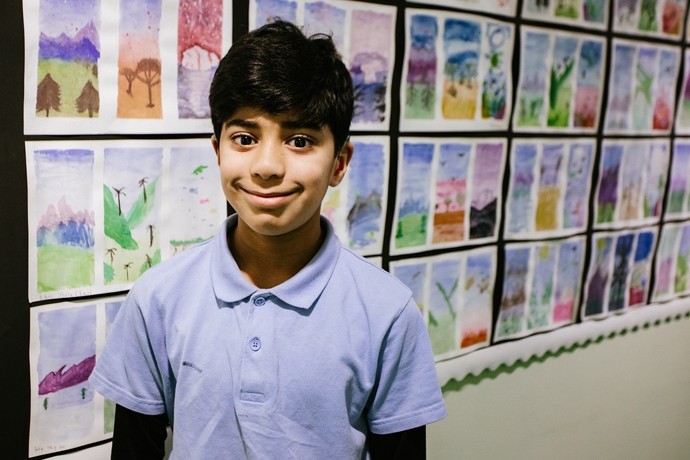 A young Asian boy standing proudly smiling in front of art work on display