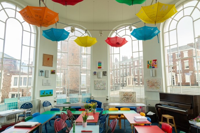 A classroom with large bay windows and colourful displays on the wall and umbrellas hanging from the ceiling 