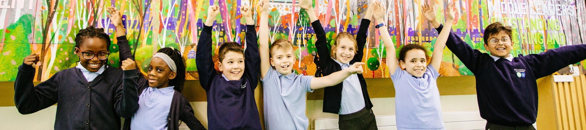 Young pupils standing in front of a colourful wall mural with their hands in the air 