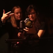 An image of two young females, stoof behind a digital camera looking intently into what they can see. 