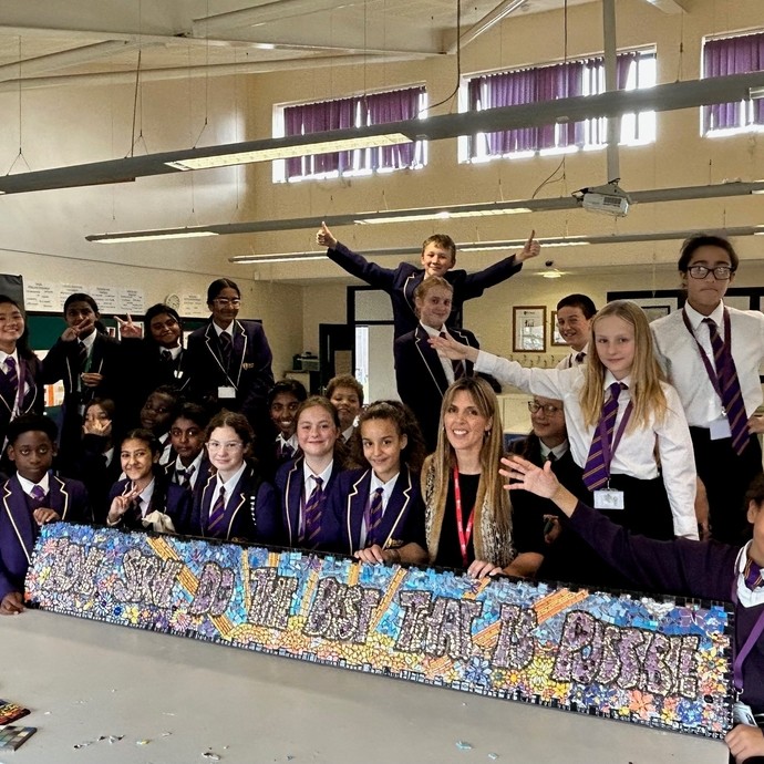 A group of Year 7 and 8 students in school uniform smiling while standing round a mosaic.
